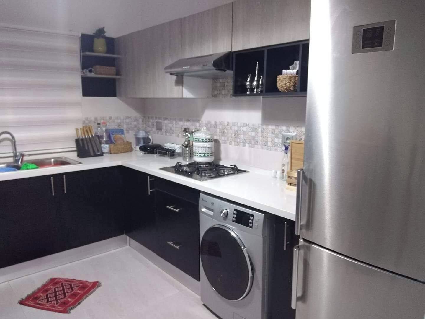 A modern kitchen with a stainless steel refrigerator, a built-in washing machine, and a gas stove.