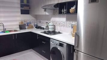 A modern kitchen with a stainless steel refrigerator, a built-in washing machine, and a gas stove.