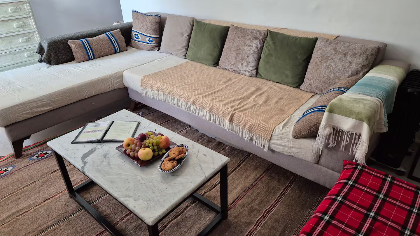 Una sala de estar con un sofá, una mesita de centro con frutas y galletas, y una manta a cuadros rojos.