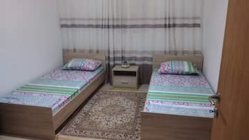 A bedroom with two wooden beds, a small bedside table, and a patterned rug.