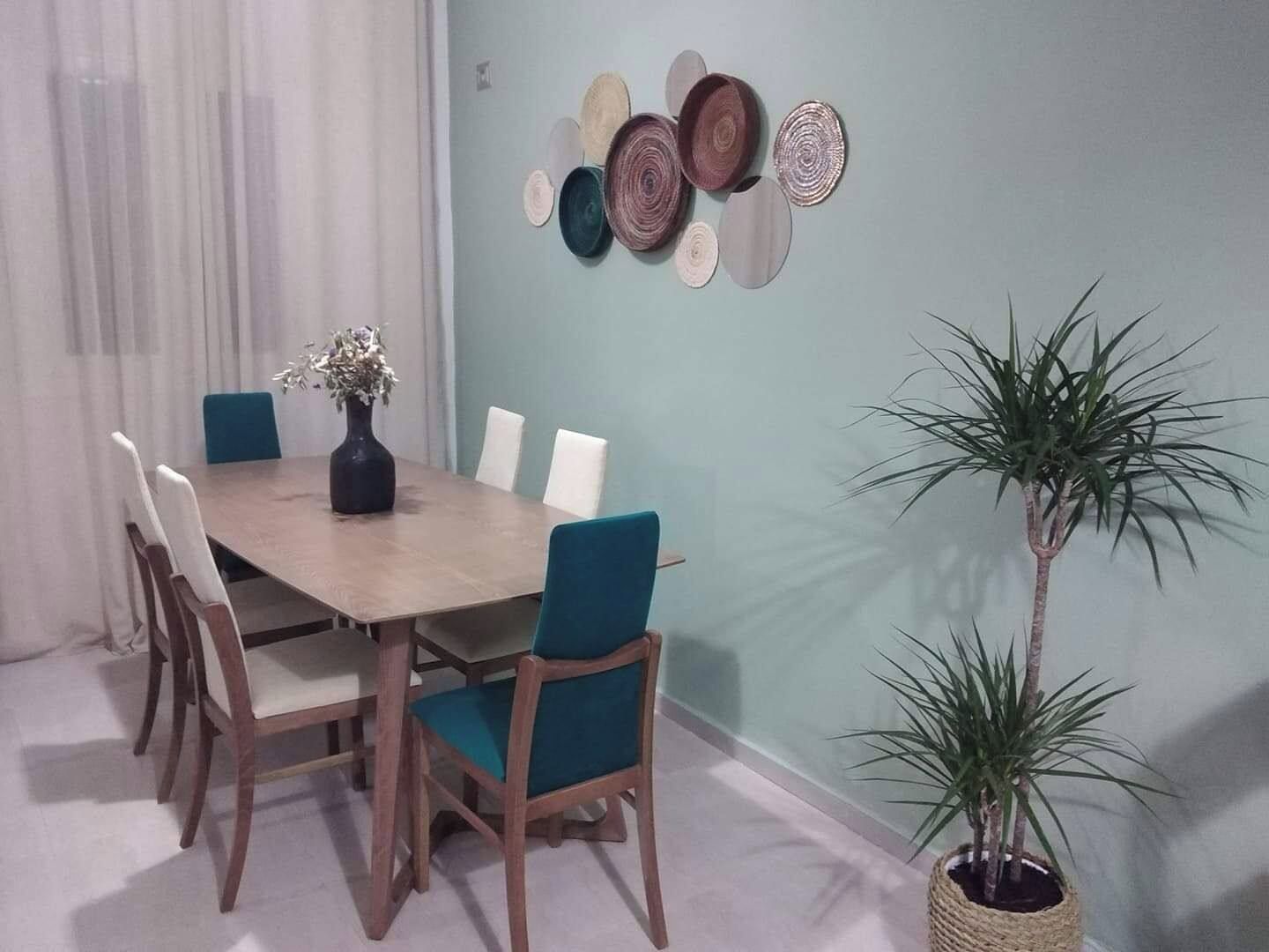 A dining area with a wooden table, six chairs, a vase with flowers, and a wall-mounted decorative plate arrangement.