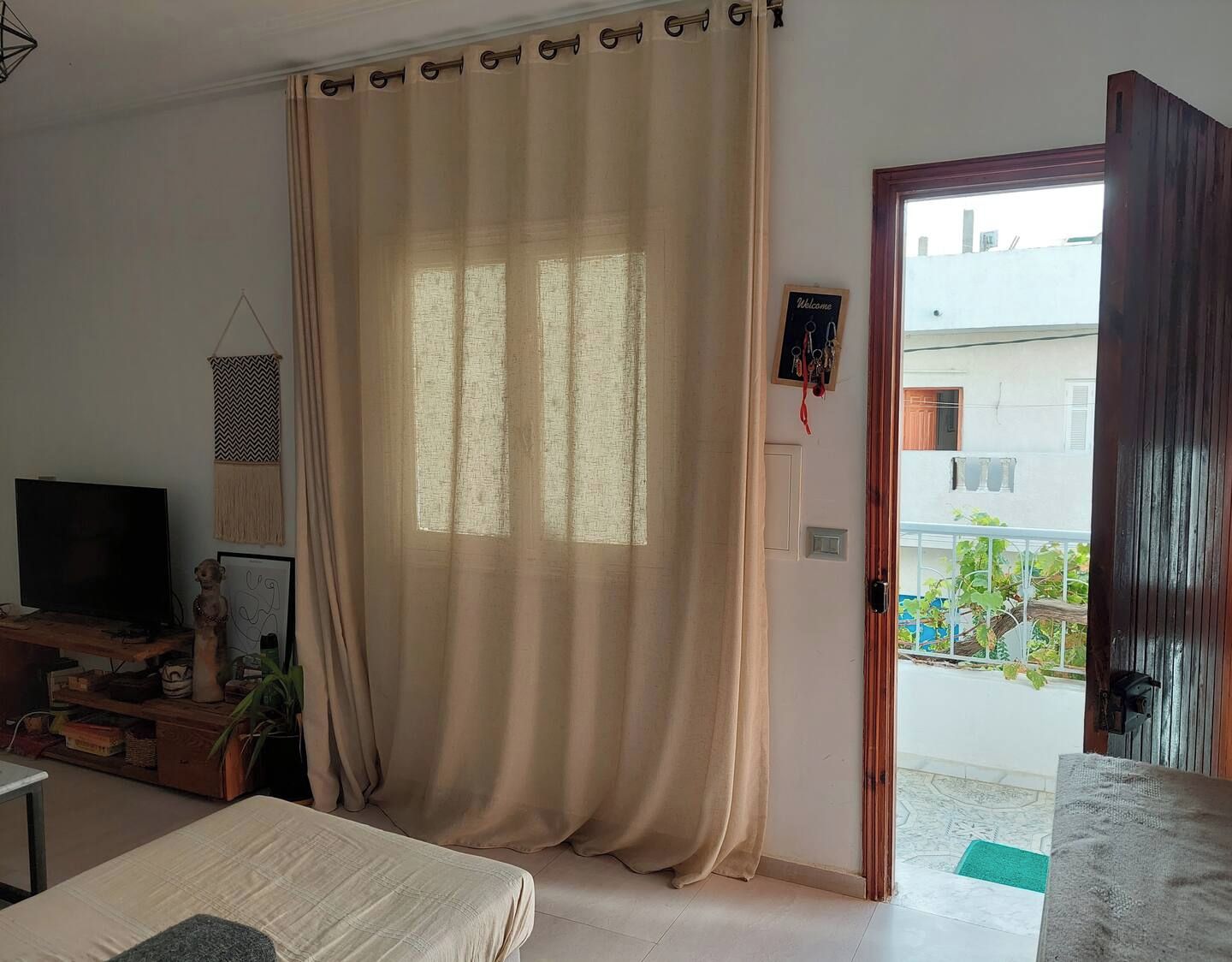 Habitación con cama, televisión, estante en la pared, puerta que da a un balcón y ventana con cortinas.