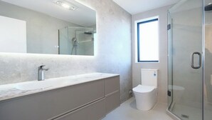 Ein modernes Badezimmer mit Duschkabine aus Glas, einer weißen Toilette und einem großen Spiegel über einer Marmorplatte.