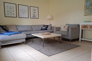 A living room with a grey sofa, a white coffee table, and a grey rug. There are framed pictures on the wall and a lamp. - Holiday home Butterfly (Plau am See)