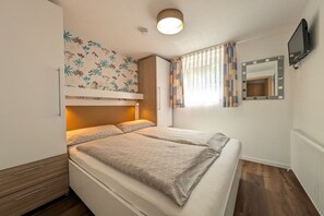 Ein Schlafzimmer mit einem Bett, einem Nachttisch, einem Spiegel und einem an der Wand befestigten Fernseher.