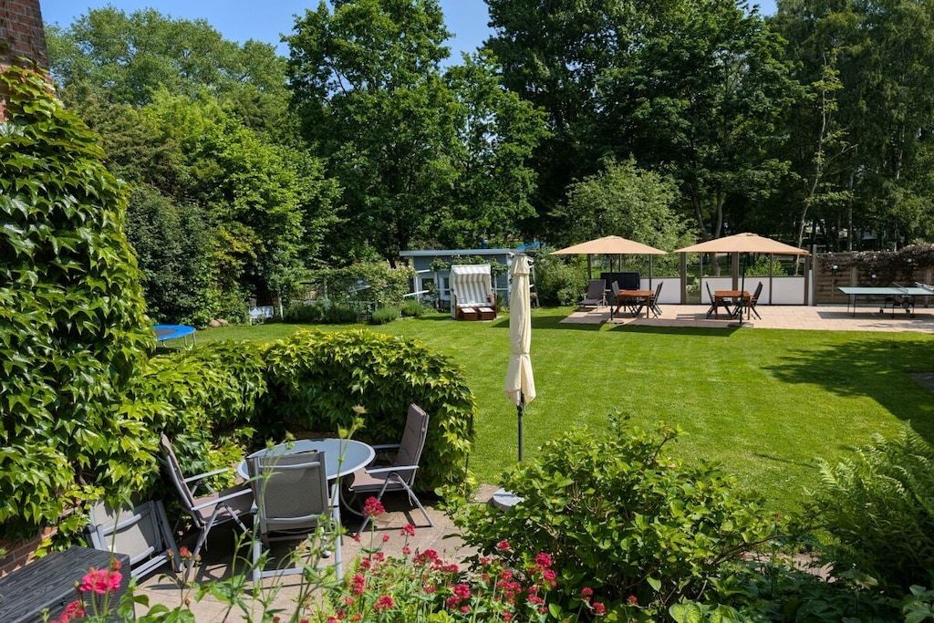 Ein Garten mit Rasen, einer Terrasse mit Tischen und Stühlen sowie einem überdachten Sitzbereich.