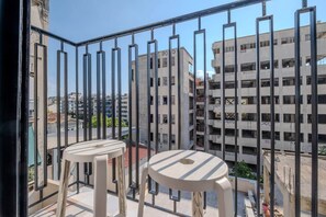 A balcony with two white plastic stools and a metal railing overlooking a cityscape with multi-story buildings. - Fun Studio for urban Explorers next to Acropolis (Athens)