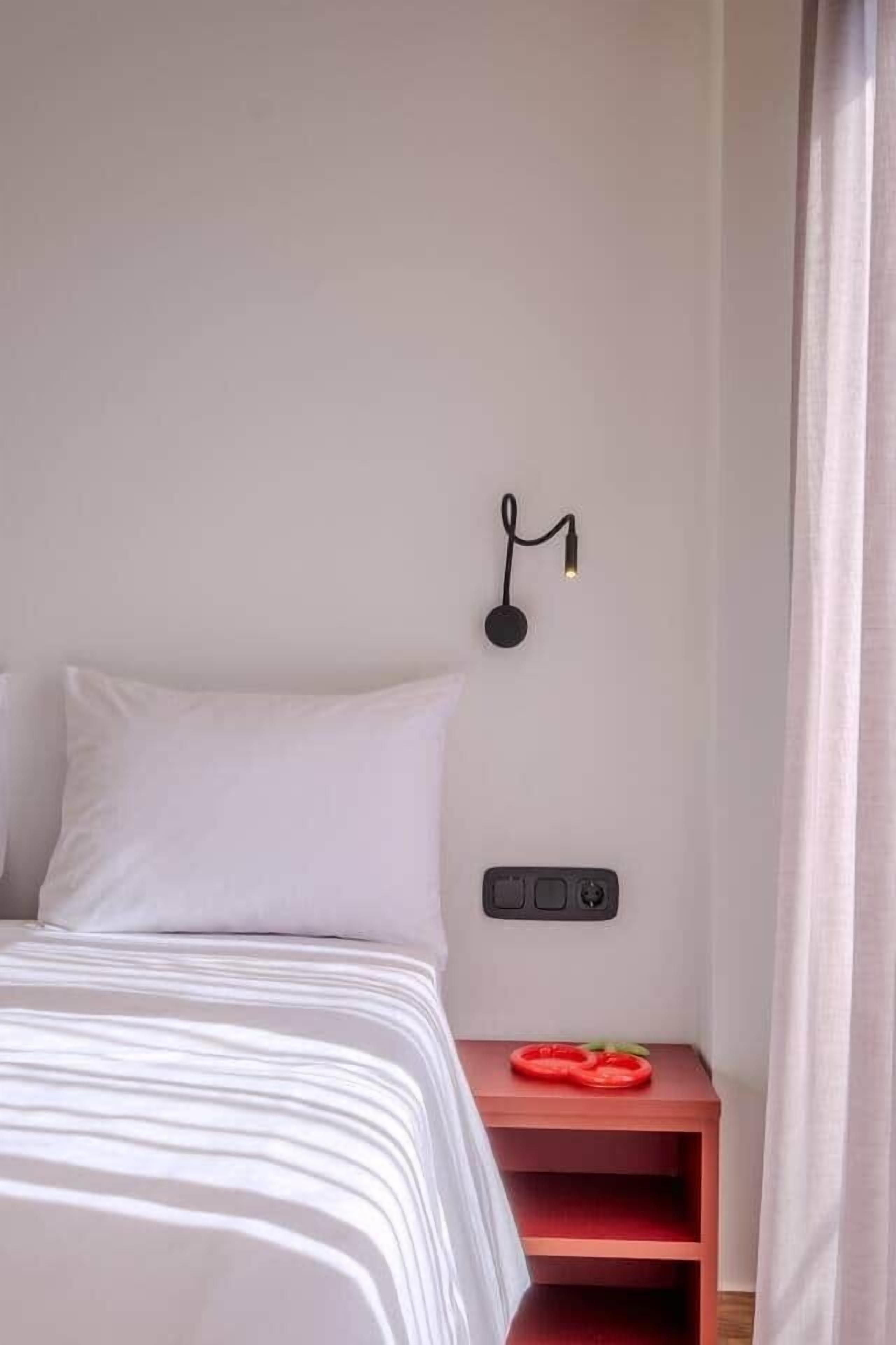 A neatly made bed with a white comforter and a red nightstand with a red object on it.
