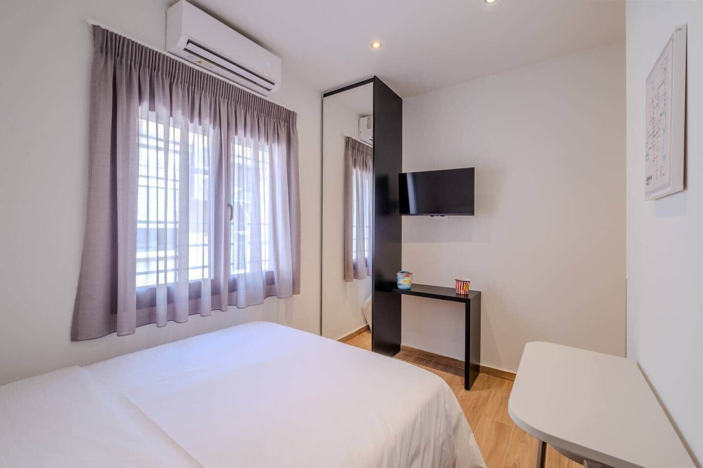 Habitació d'hotel amb un llit, un televisor fixat a la paret, una taula petita amb una tassa i un aparell d'aire condicionat.