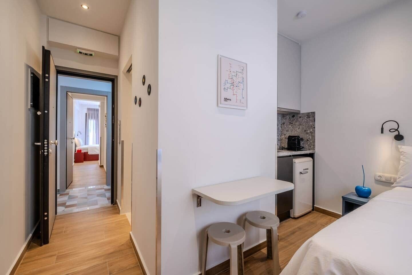 A hotel room with a bed, a small kitchenette, a desk, and a bathroom visible through an open door.