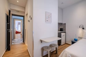 A hotel room with a bed, a small kitchenette, a desk, and a bathroom visible through an open door. - Fun - Sized Design studio next to Acropolis (Athens)