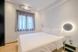 Ett hotellrum med en säng, en luftkonditioneringsanläggning, ett nattduksbord med en klocka och en väggmonterad lampa.