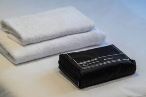 A neatly folded white towel and a black toiletry bag on a bed. - Pop Urban Escape near the center (Athens)