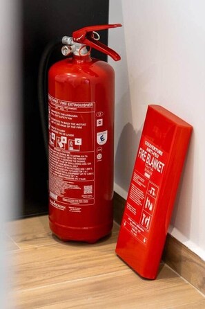 A red fire extinguisher and a red fire blanket on a wooden floor. - Playful Design close to Athens Highlights (Athens)