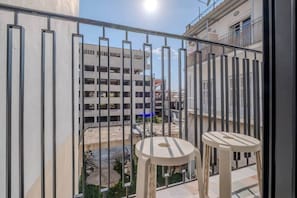 A balcony with a metal railing, two beige chairs, and a view of a building with multiple windows and balconies. - Tiny colorful studio near the Historic Center (Athens)
