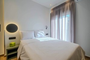 A modern hotel room with a large bed, a bedside table, a wall-mounted light, and a window with curtains. - Tiny colorful studio near the Historic Center (Athens)