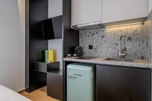 A compact kitchenette with a built-in refrigerator, a sink, and a stove. - Tiny colorful studio near the Historic Center (Athens)