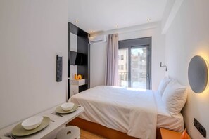 A modern hotel room with a bed, a bedside table with plates, a flat-screen TV, and a window with a view of buildings. - Color Pop Studio with city Vibes near Center (Athens)
