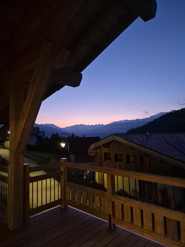A wooden deck with a railing overlooking a mountainous landscape during twilight.
