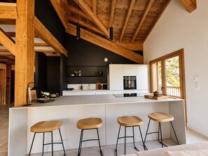 A modern kitchen with a central island, bar stools, and a view of the outdoors through a window.