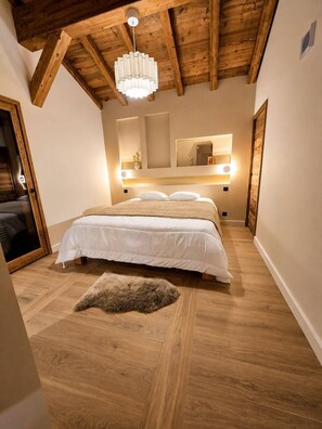 A bedroom with a wooden ceiling, a bed with white bedding, a fluffy rug, and wall-mounted lighting.