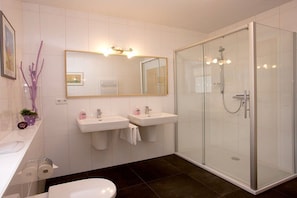 Une salle de bain moderne avec deux lavabos, des toilettes, un espace douche et un miroir avec éclairage intégré.