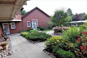 Il s’agit d’une propriété résidentielle comprenant une maison en briques, une allée pavée et un jardin agrémenté de diverses plantes et fleurs.