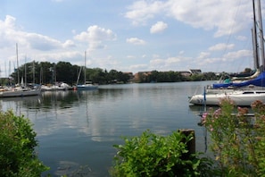 A marina with boats docked, calm water, and greenery in the foreground.