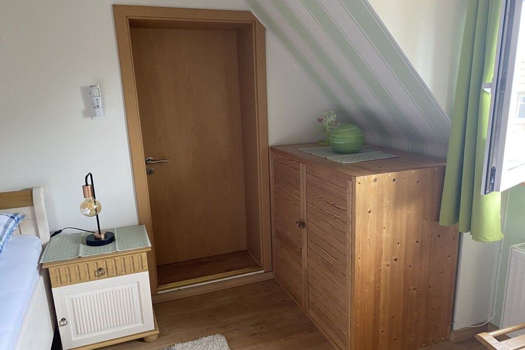 Een slaapkamer met een houten garderobe, een nachtkastje met een lamp, een radiator en een raam met gordijnen.