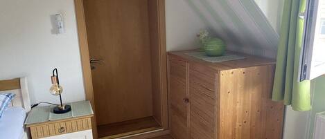 Een slaapkamer met een houten garderobe, een nachtkastje met een lamp, een radiator en een raam met gordijnen.