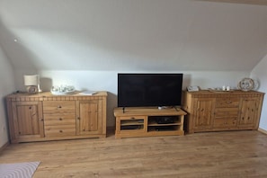 A room with a wooden cabinet, a television, and a small table with a lamp and decorative items.