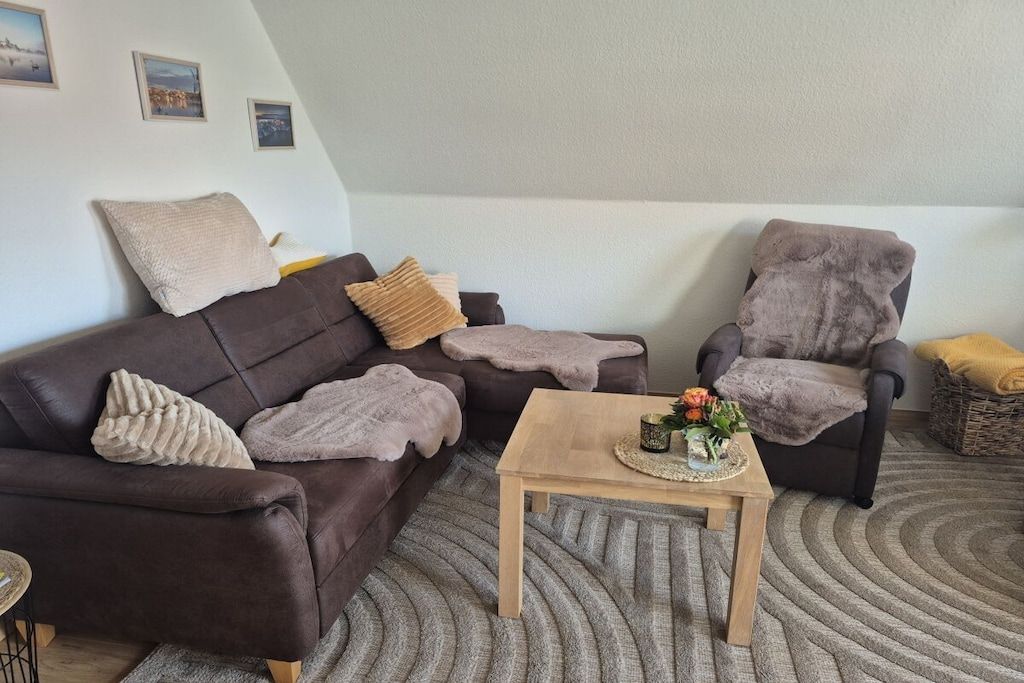 A living room with a brown sofa, a grey armchair, a wooden coffee table, and a grey rug.