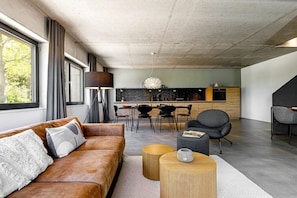 A modern living room with a leather sofa, a dining area with chairs, and a kitchen in the background. - Holiday home in Fehmarn with swimming pool (Fehmarn)