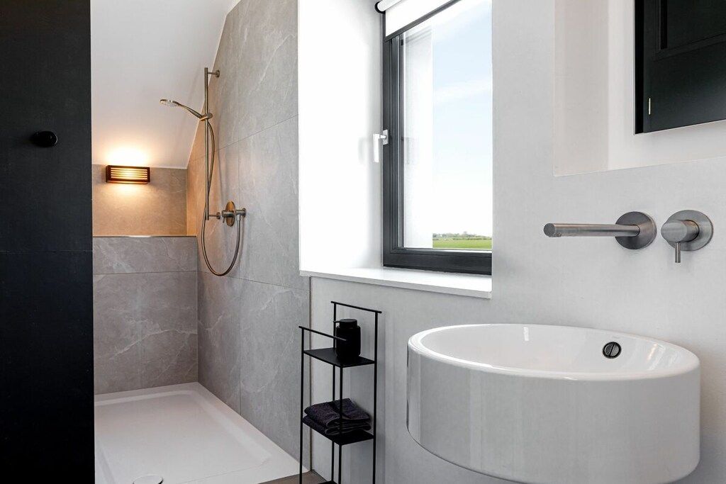 A modern bathroom with a large sink, a shower, and a window providing natural light.