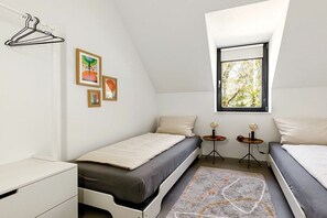 A small, modern bedroom with two single beds, a white dresser, a window with a view of trees, and a wall-mounted coat rack. - Holiday home in Fehmarn with swimming pool (Fehmarn)