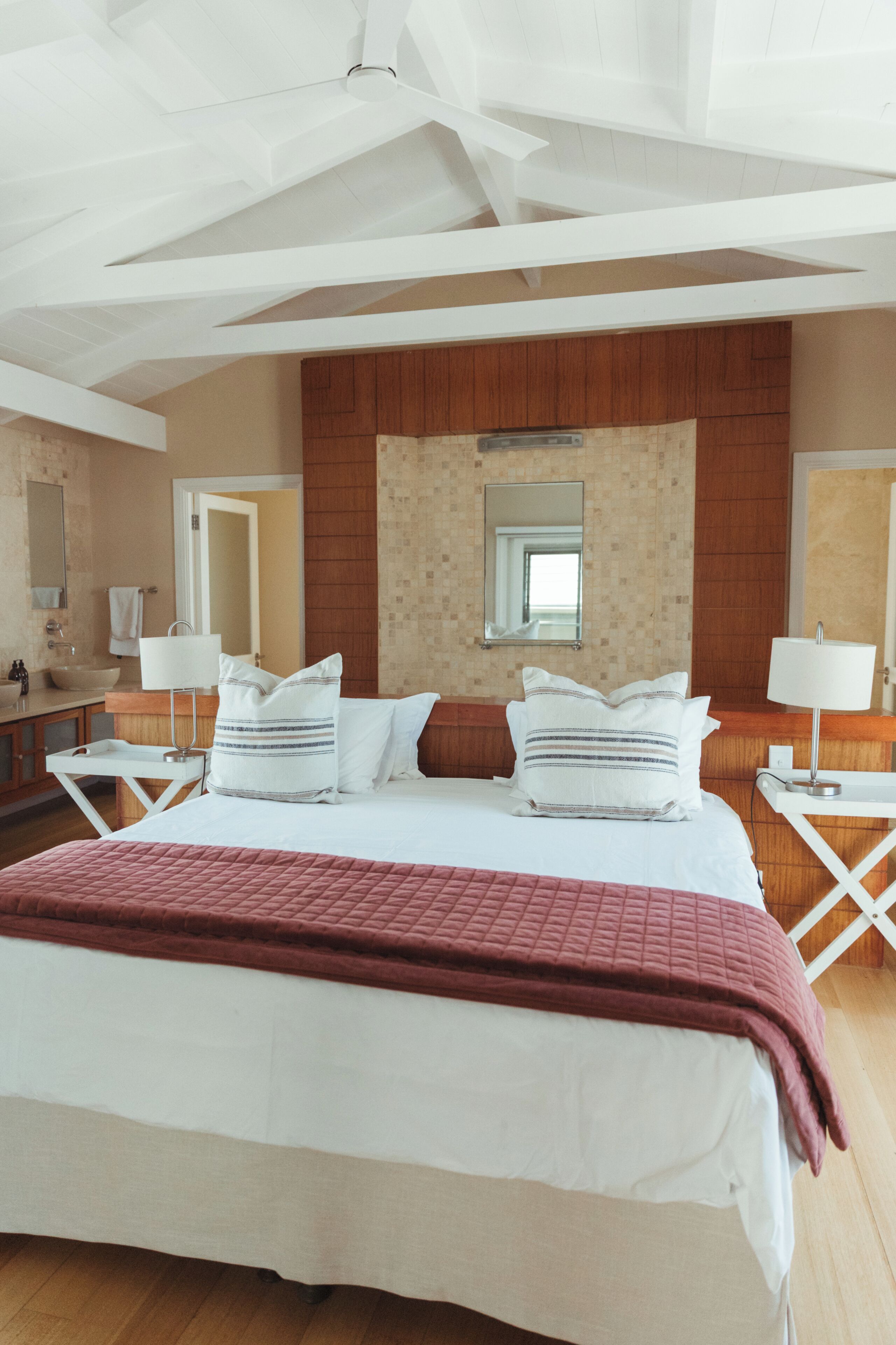 A hotel room with a large bed, two bedside tables, a mirror, a wooden panel wall, and a ceiling fan.