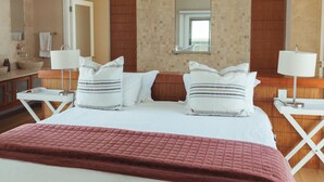 Une chambre d’hôtel avec un grand lit, deux tables de chevet, un miroir, un mur recouvert de panneaux en bois et un ventilateur de plafond.