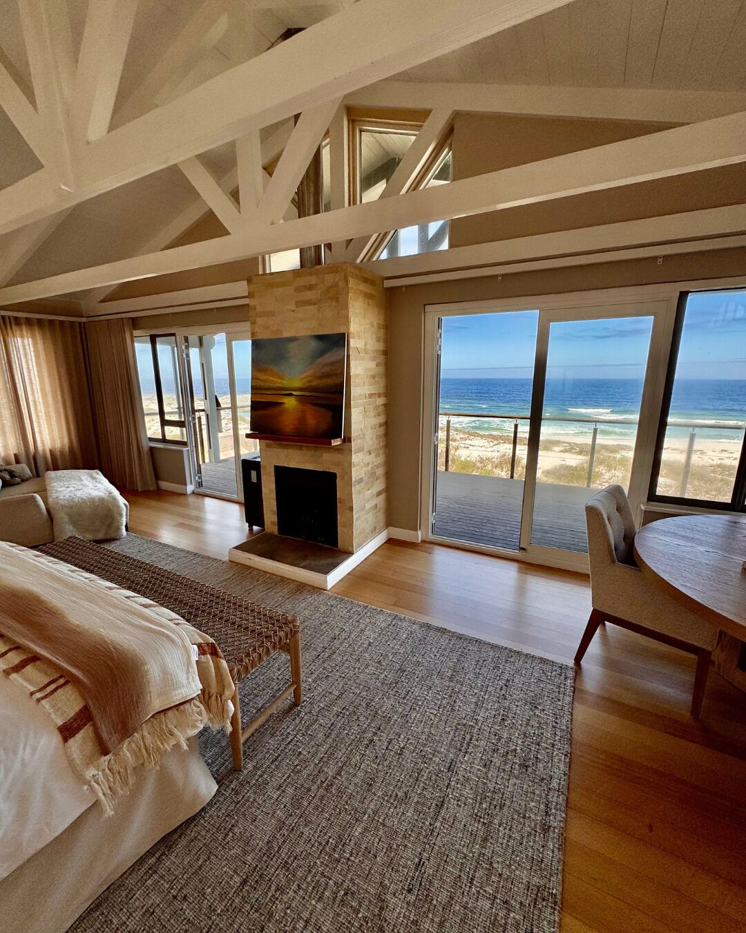 A spacious room with a large bed, a fireplace, a dining area, and a balcony with a view of the ocean.