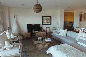 Una sala de estar con sofá, sillones, una mesa de centro, televisión y obras de arte en la pared.