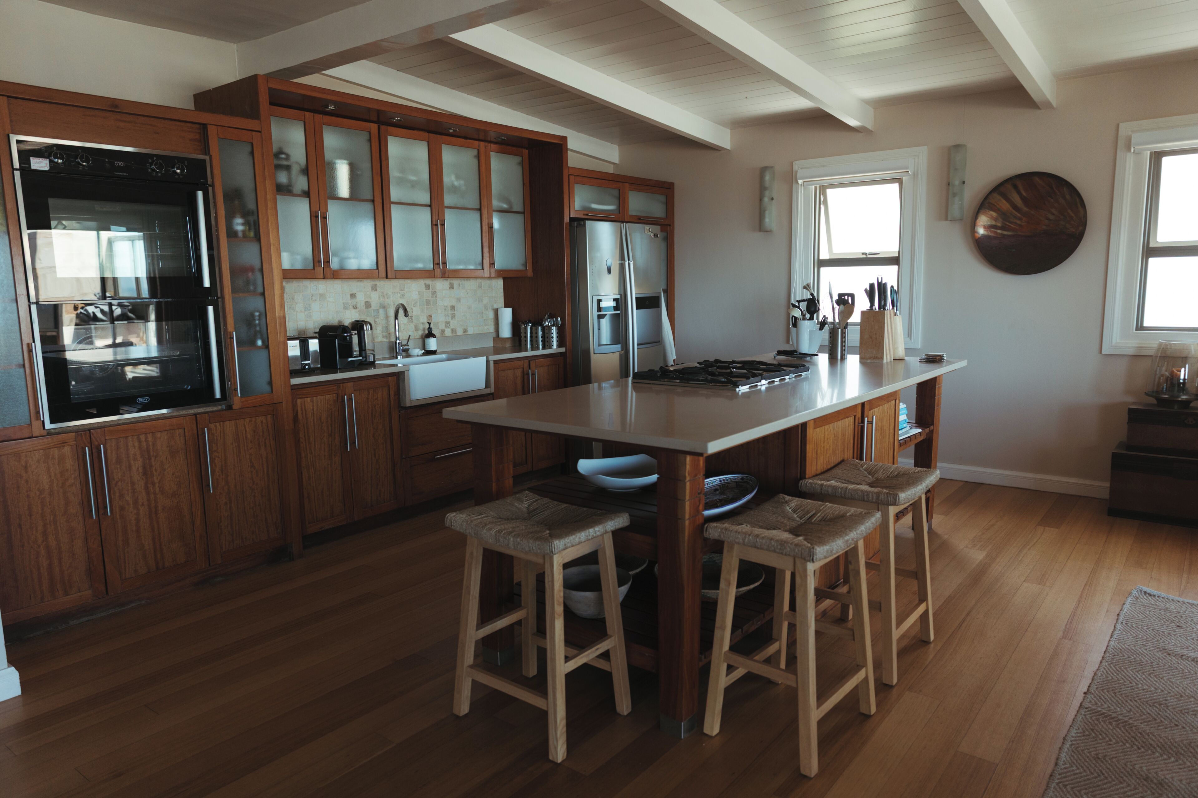 A kitchen with wooden cabinets, a stainless steel refrigerator, a double sink, and a large island with stools.