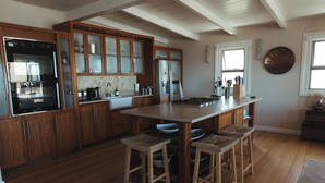 Une cuisine avec des meubles en bois, un réfrigérateur en acier inoxydable, un évier à deux bacs et un grand îlot central doté de tabourets.