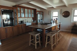A kitchen with wooden cabinets, a stainless steel refrigerator, a double sink, and a large island with stools. - Luxury 4 Bedroom Beachfront Villa/Private Pool & Ocean Views (Yzerfontein)