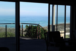 Una habitación con vista al océano, grandes ventanales, una terraza de madera y una silla.