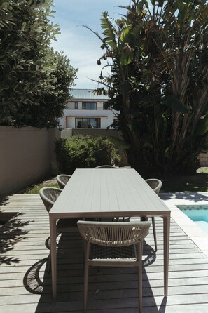 An outdoor patio with a table and chairs, surrounded by lush greenery and a view of a modern building.