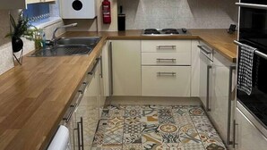 Cocina compacta con estufa a gas, horno integrado, extractor de acero inoxidable y piso de baldosas estampadas.