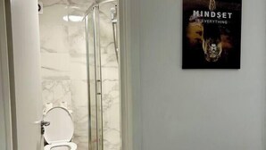 Un baño con cabina de ducha de vidrio, inodoro y un cartel en la pared.