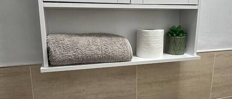 Un baño con un lavamanos blanco, un armario espejo y una repisa con una toalla y una planta pequeña.