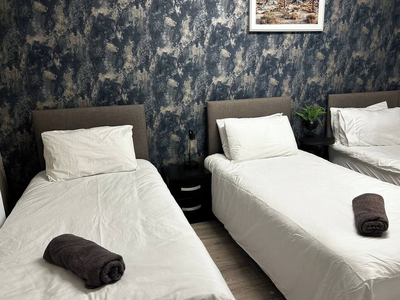 A hotel room with two beds, white bedding, and a dark textured wall.