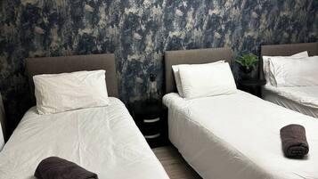 A hotel room with two beds, white bedding, and a dark textured wall.