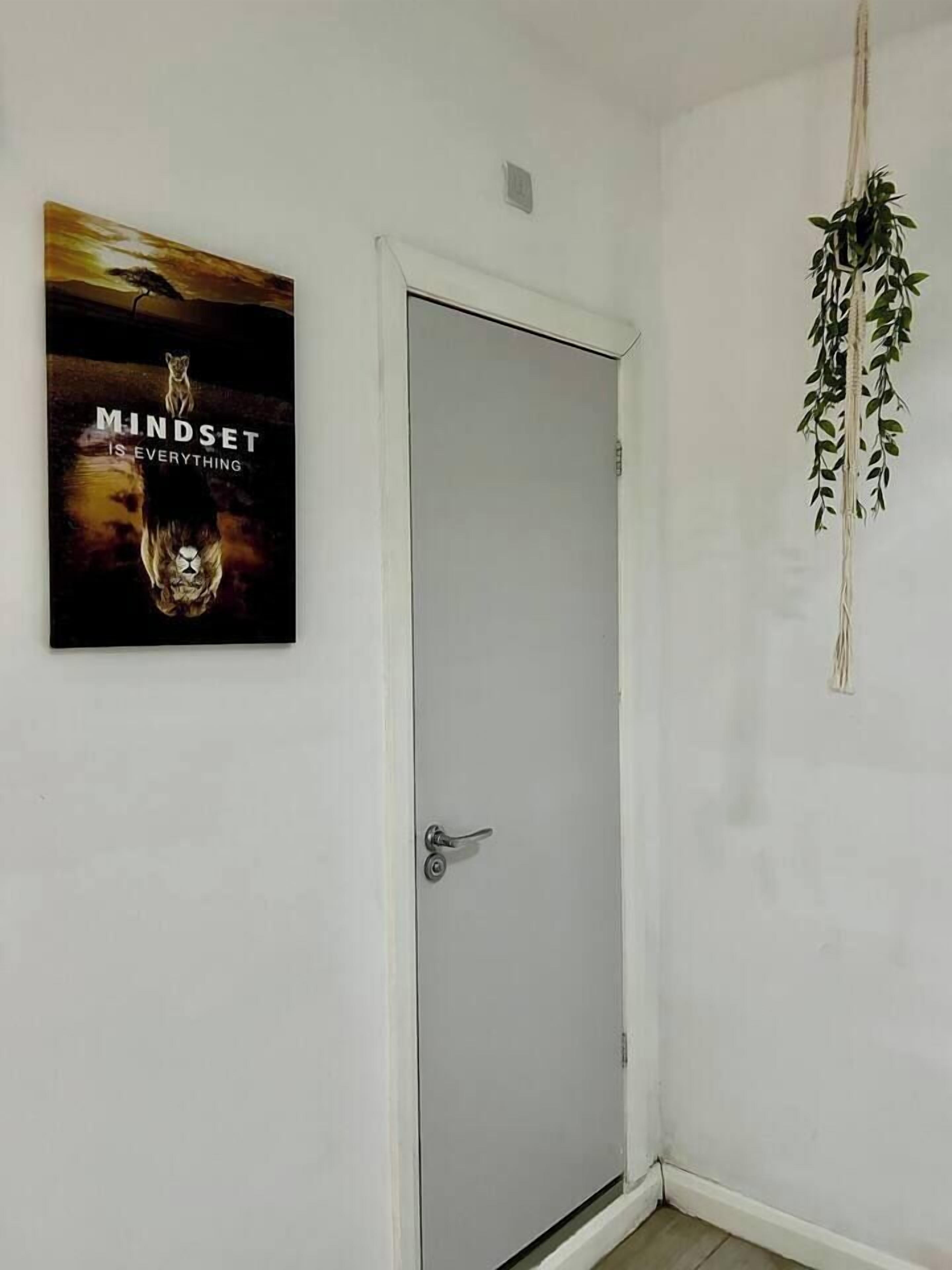 A white door with a silver handle, a framed motivational poster on the wall, and a hanging plant.